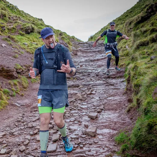 A marathon runner on the beacons ultra, pulling a hang ten sign and sticking his tongue out